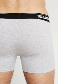 Graue Baumwollboxershorts mit einem schwarzen Bund, auf dem "URBAN CLASSICS" in Weiß steht. Der Stoff ist glatt und dehnbar für zusätzlichen Komfort.