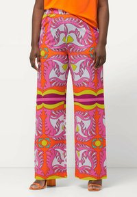 Kleurige wijde broek met een bloemenpatroon in roze, oranje en geel, gemaakt van lichtgewicht stof. Gecombineerd met oranje blokhak sandalen.