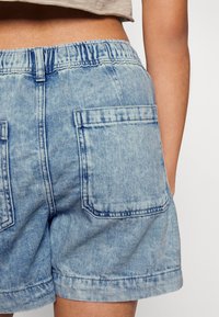 Světle modré džíny šortky s elastickým pasem, které mají dvě zadní kapsy a mírně opotřebovaný vzhled. Lem je ohrnutý.
