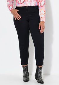 Schwarze Jeans mit schlanker Passform, die eine mittelhohe Taille und fünf Taschen aufweisen, kombiniert mit genoppten schwarzen Knöchelschuhen.