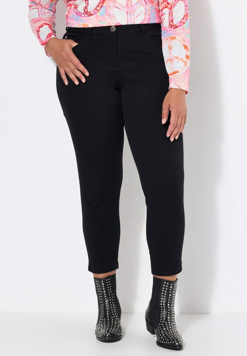 Schwarze Jeans mit schlanker Passform, die eine mittelhohe Taille und fünf Taschen aufweisen, kombiniert mit genoppten schwarzen Knöchelschuhen.