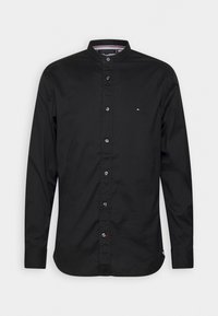 Camisa negra de algodón con cuello y botones, con mangas largas, tapeta frontal y un pequeño detalle de logo en el pecho.