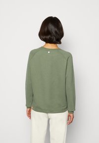 Sudadera verde oliva con mangas raglán, textura suave y un pequeño detalle de logo en la parte posterior cerca del cuello. De ajuste ligero y casual.