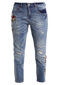 Jeans bleus pour femmes, déchirés, avec broderies florales sur la cuisse et le mollet, présentant un détail de poche à clous bleu foncé.