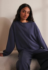 Oversized donkerpaars sweatshirt met een ronde halslijn en verlaagde schouders, gecombineerd met bijpassende broek. Zachte stof met minimale naden.