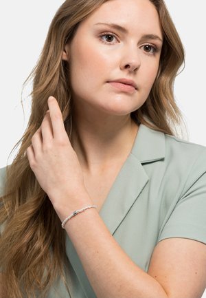 Klarer, perlenschnurarmband mit transparenten Perlen und einer zentralen dunklen Perle. Modell trägt ein hellgrünes, mit Kragen versehenes Oberteil und spielt mit ihren Haaren.