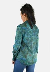 Camisa verde con estampado paisley, de mangas largas, con botones en la parte frontal y dobladillo curvado. El material parece suave con una textura sedosa.
