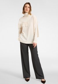 Vaalean kerma sävyinen neulepaita, jossa on korkea kaulus ja fringed yksityiskohtia, yhdistetty tummanharmaisiin, leveälahkeisiin housuihin. Pehmeä neuletekstuuri ja rento malli.