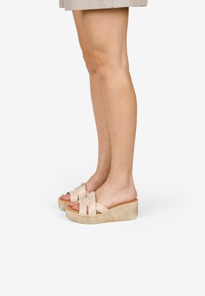 Sandalias de cuña beige con suelas de cuerda trenzada, que presentan un diseño de tiras cruzadas en material suave. Estilo de punta abierta y sin respaldo para fácil uso.