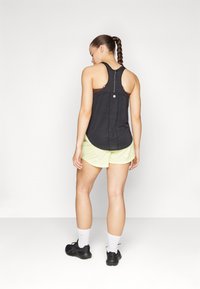 Black athletic tank top with a racerback design and back button detail, paired with light green shorts and black running shoes.