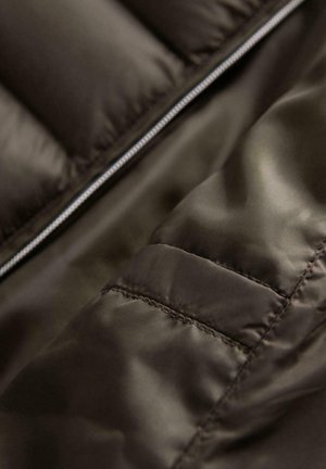 Dunkelbrauner Steppjackenstoff mit einer glatten Textur, sichtbaren Nähten und einem Reißverschluss, der einen Nahaufnahm des Materials zeigt.