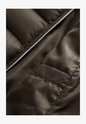 Dunkelbrauner Steppjackenstoff mit einer glatten Textur, sichtbaren Nähten und einem Reißverschluss, der einen Nahaufnahm des Materials zeigt.