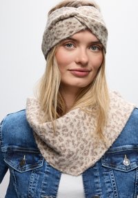 Fascia in maglia color beige con design attorcigliato, abbinata a una sciarpa beige coordinata con un morbido motivo leopardato, indossata con una giacca di jeans.