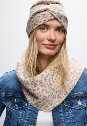 Strikket pandebånd i beige med et snoet design, parret med et matchende beige tørklæde med et blødt leopardmønster, båret med en denimjakke.
