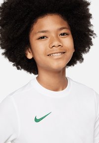 Maglietta atletica bianca con collo tondo, dotata di un logo Nike ricamato verde sul lato sinistro del petto. Tessuto liscio e leggero.