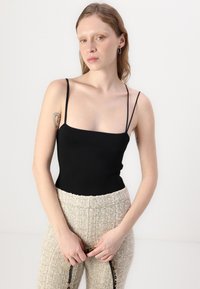 Svart tettsittende tank topp med tynne stropper, kombinert med strukturerte beige høyt livbukser, holdt oppe med et mønstrete belte.