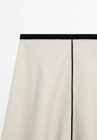 Tissu beige clair avec une ceinture noire et une couture noire verticale au centre.