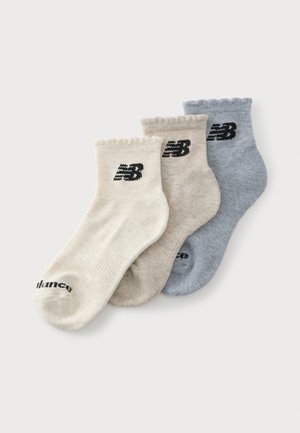 Trzy pary skarpetek do kostki w kolorach kremowym, beżowym i niebieskim z czarnymi logo New Balance na każdym mankiecie i palcu.
