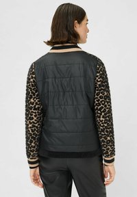 Zwarte gewatteerde bodywarmer met mouwen in luipaardprint. Beschikt over gestreepte boorden, een gladde textuur op het lichaam en een pluizige textuur op de mouwen.
