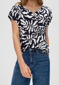 Haut à manches courtes bleu marine avec un motif abstrait blanc, design à col en V et finition texturée, associé à un jean en denim taille haute.