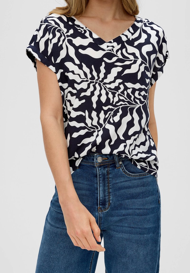 Haut à manches courtes bleu marine avec un motif abstrait blanc, design à col en V et finition texturée, associé à un jean en denim taille haute.