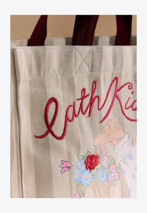 Geantă tote bej în dungi cu mânere burgundy, text brodat roșu „Cath Kid” și ilustrație cu un câine care ține un coș cu flori.