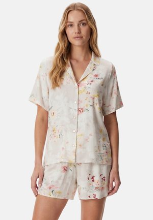 Ung kvinde iført en lysefarvet kortærmet knap-op skjorte og matchende shorts med et delikat blomstermønster.