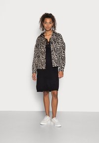 Leopardmønstret, oversized jakke lavet af blødt stof, lagdelt over en sort, ærmeløs strikkjole. Sæt med hvide sneakers.