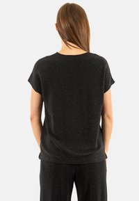 Top negro de manga corta fabricado en una tela texturizada y brillante. Presenta un escote redondo y un corte relajado en la parte trasera.