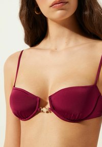 Bordeaux bikini top med justerbare stropper, underwire støtte, sammenkrøbet stof og en guldfarvet hardware detalje i midten.