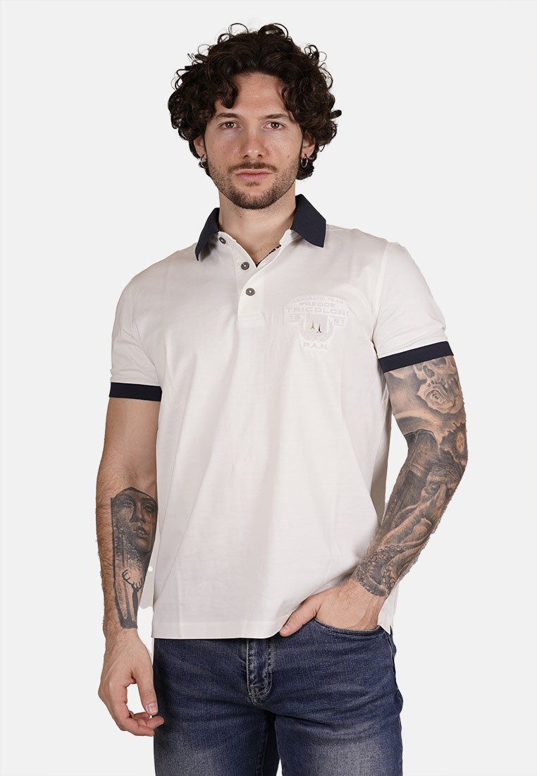 Polo in cotone bianco con colletto e polsini blu navy, caratterizzato da un logo sul petto e una patta con due bottoni. Indossato con jeans scuri.