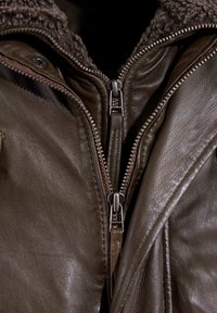Bruine leren jack met een gestructureerde kraag, dubbele ritssluitingen en zichtbare stiksels. Voorzien van een gladde afwerking en een gezellige binnenvoering.