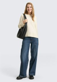 Maglione a maglia beige chiaro con orlo a coste, abbinato a jeans a gamba larga blu scuro e borsa in pelle nera, indossato con scarpe nere chunky.