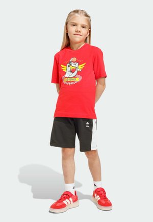Röd bomulls-t-shirt med grafiskt tryck, svarta shorts med vita detaljer och röda sneakers med vita ränder. Avslappnad sportklädsel för barn.