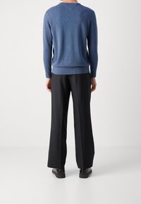 Niebieski sweter dzianinowy z dekoltem w serek, w połączeniu z czarnymi spodniami o szerokich nogawkach i czarnymi butami, widziany z tyłu. Widoczna gładka tekstura.