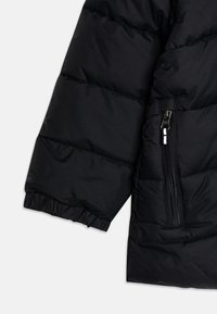 Schwarze Pufferjacke mit gesteppten Abschnitten am Ärmel, elastischem Bündchen und einer Reißverschlusstasche mit silbernem Reißverschluss und Stoffstruktur.