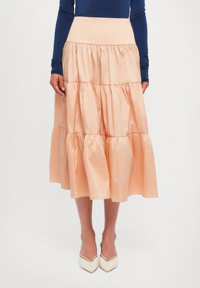 Jupe midi en pêche à volants avec une large ceinture élastique. Fabriquée en tissu léger avec une texture lisse. Associée à des talons aiguilles crémeux.