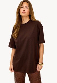 T-shirt en coton marron à coupe décontractée, manches courtes et encolure ronde, avec une texture douce et des détails de design simples.