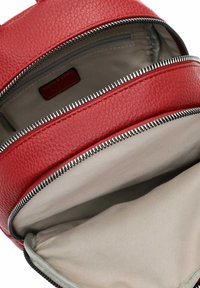 Zaino in pelle rossa con superficie texture, dotato di numerosi scomparti con zip e fodera in tessuto grigio all'interno.