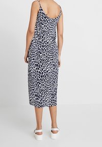 Granatowa i biała sukienka midi w wzory, z cienkimi ramiączkami, lekko dopasowana u góry, opadająca do długości kostek. Noszona z sandałami na platformie.