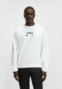 Felpa bianca con logo "BOSS" in nero sopra tre cerchi colorati. Presenta un collo a giro e polsini a costine. Abbinata a pantaloni neri.