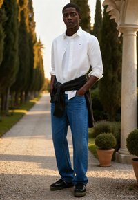 Camisa branca com botões sobre uma t-shirt branca, suéter escuro amarrado à cintura, jeans azuis e ténis pretos com detalhes verdes.