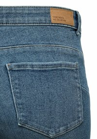 Sinised teksapüksid tagataskuga, mille vöökohal on õmmeldud nahkmärgis. Kangas on tekstuurse ja veidi tuhmunud väljanägemisega.