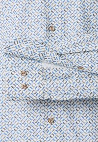 White shirt with blue and gray geometric pattern, featuring brown buttons and a folded cuff.