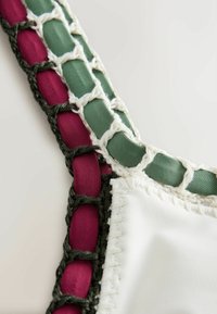 Gros plan d’un tissu blanc avec des rubans verts et rouges tissés à travers des bords en point de crochet foncés.