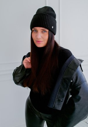Gorro de canalé negro, jersey de cuello alto negro y chaqueta de cuero negra. Tejido suave y brillante; cabello largo y liso; detalle de hardware sutil en el gorro.