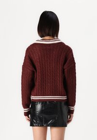 Maglione bordeaux a trecce con strisce bianche al colletto e ai polsini, abbinato a una mini gonna nera con stampa a croco.