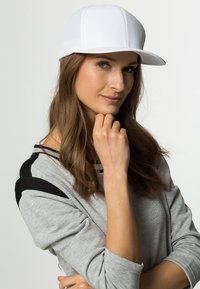 White baseball cap with a structured design, featuring a flat brim and mesh panels. Paired with a gray long-sleeve top with black accents.