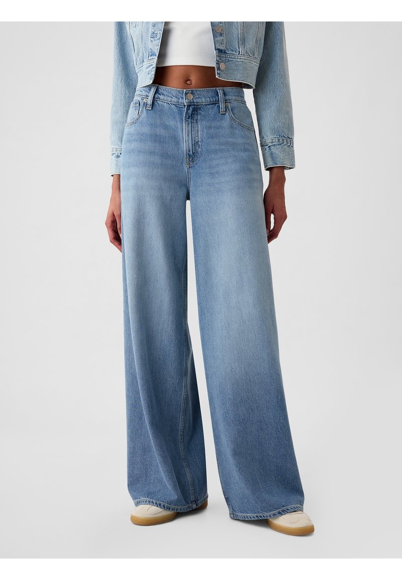 Vaaleansiniset leveälahkeiset farkut korkealla vyötäröllä, valmistettu farkkukankaasta. Ominaisuuksina edessä nappisuljenta ja hillitty haalistuminen. Yhdistetty valkoisen paidan ja beigejen kenkien kanssa.