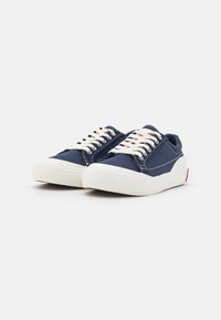 Marina canvas sneakers med vit gummisula, snörning fram, kontrasterande sömmar och röd accent på hälen.